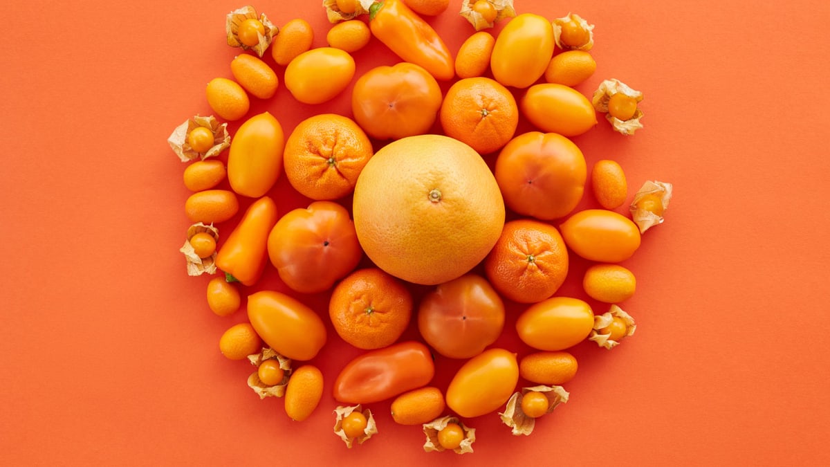 Bright flat lay of assorted citrus fruits and vegetables on an orange background, showcasing vivid colors and freshness.