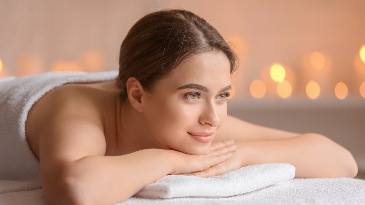 A serene woman enjoying a spa experience with flickering candles, wrapped in a towel, portraying pure relaxation.